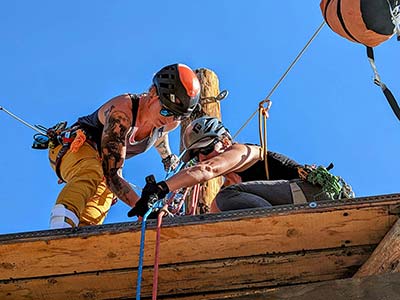 Two people wearing helmets and rope gear and harnesses fix rope gear on a platform